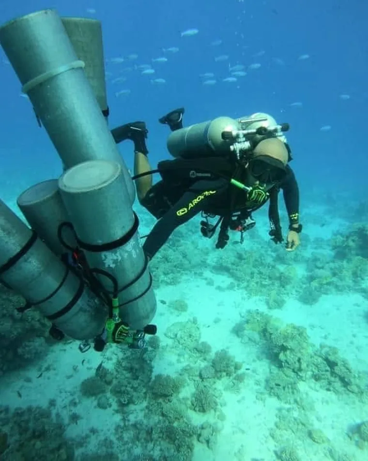 Technical diver carrying a stage cylinder over the reef